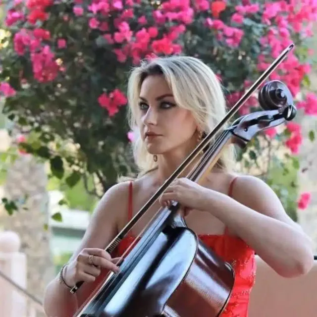 Cellist in a red dress playing outdoors in front of bougainvillea