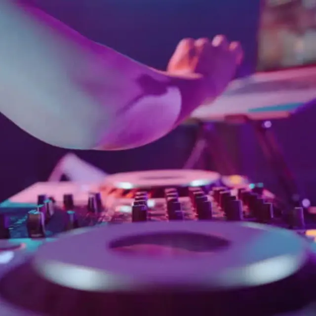 DJ’s hand on a mixer under purple light