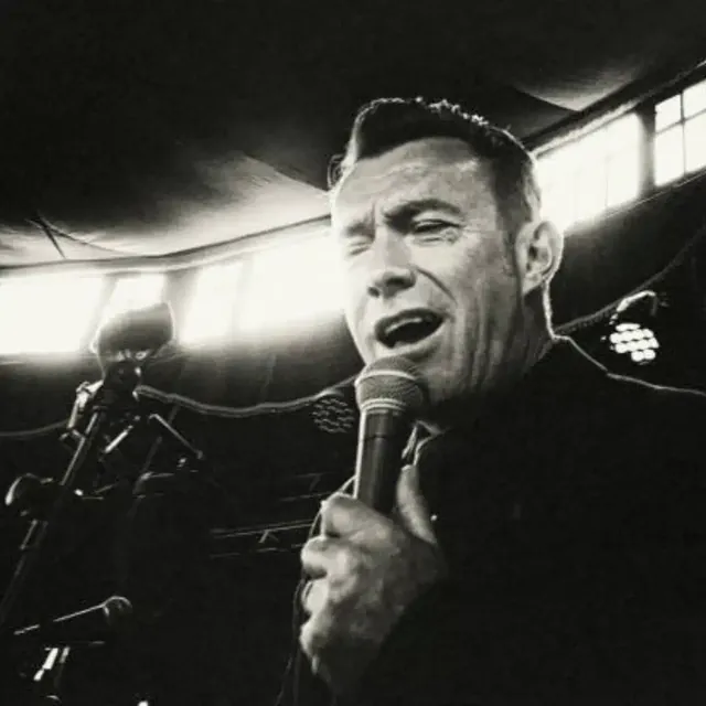 Black-and-white photo of a male singer performing at a microphone