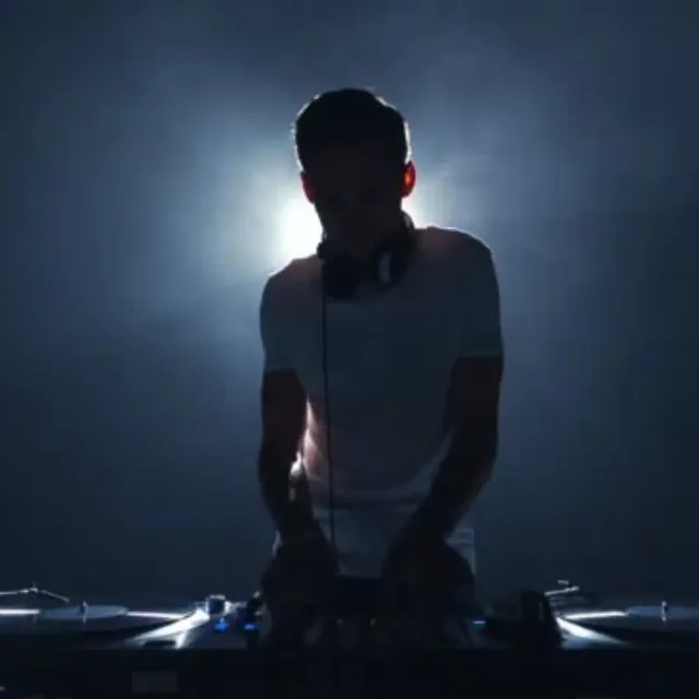 DJ in silhouette behind decks with stage light behind him