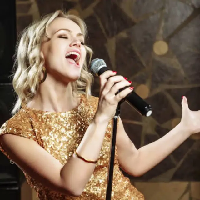 Singer in a gold sequinned dress singing into a microphone