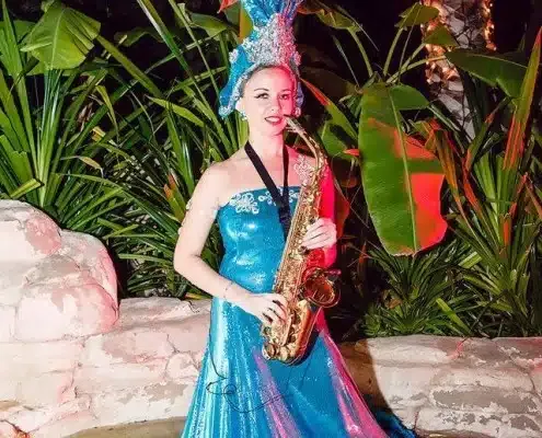 Saxophonist in a turquoise gown and feathered headpiece in a tropical garden