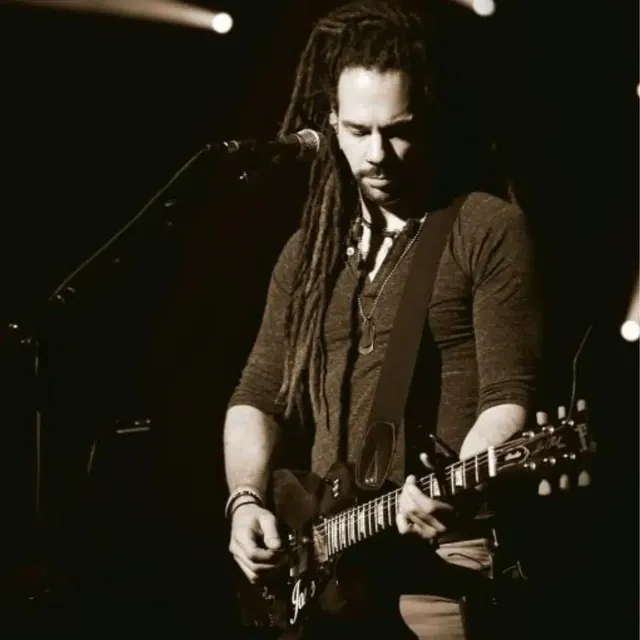 Singer with dreadlocks playing electric guitar on stage