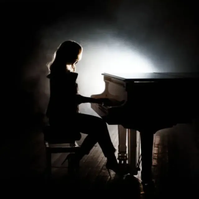 Female pianist in silhouette at a grand piano under a single spotlight