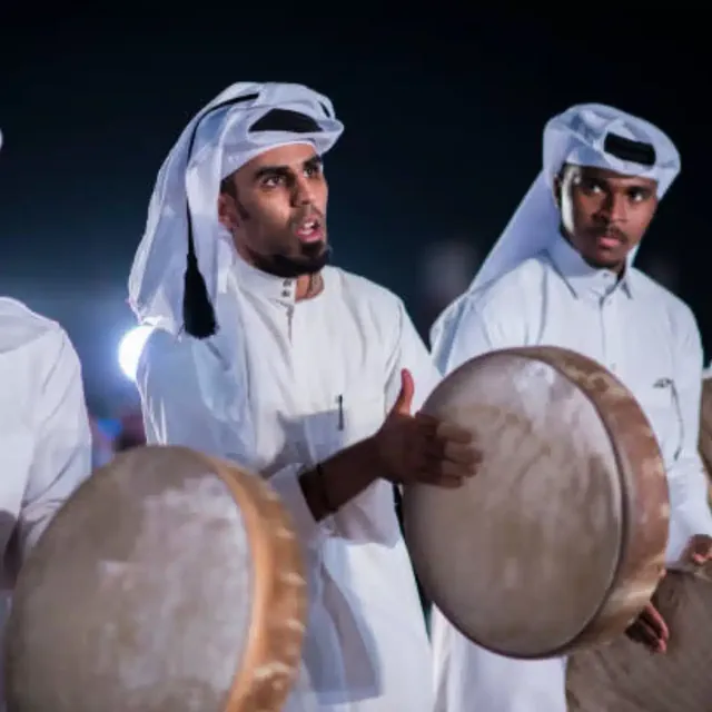 Musicians in white ghutra playing frame drums at night