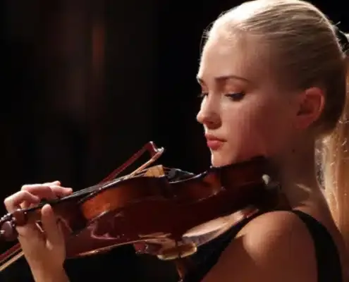 Violinist with her eyes lowered, playing against a dark background